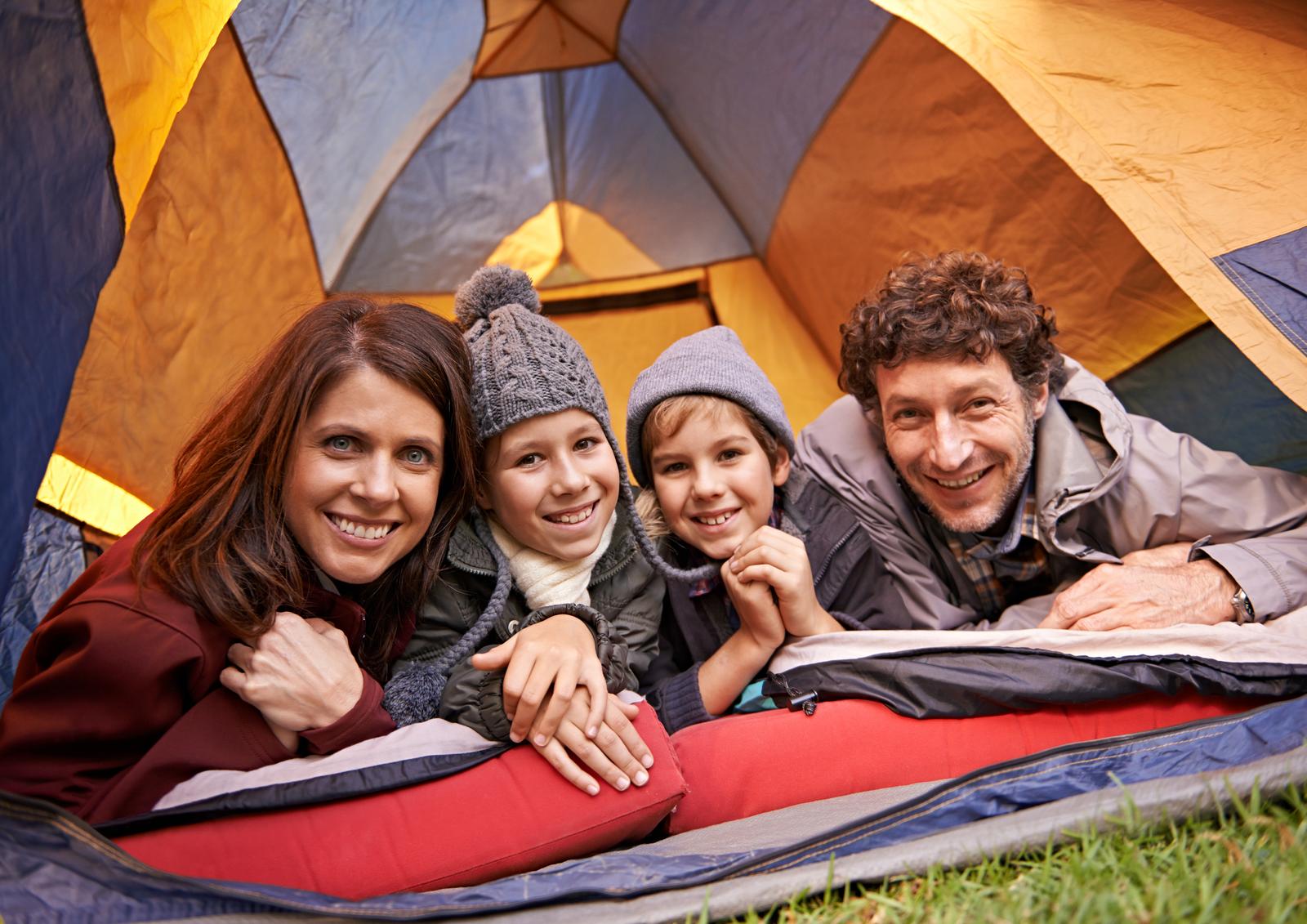Portrait of smiling family of four relaxing in tent on a camping holiday.